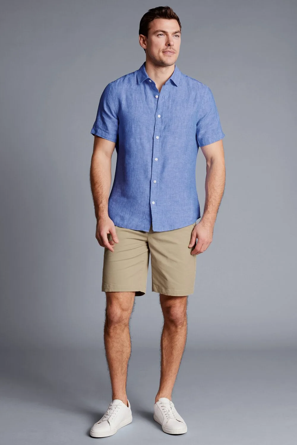 A man wearing a blue short-sleeve linen shirt and brown chino shorts — a relaxed, lightweight summer outfit.