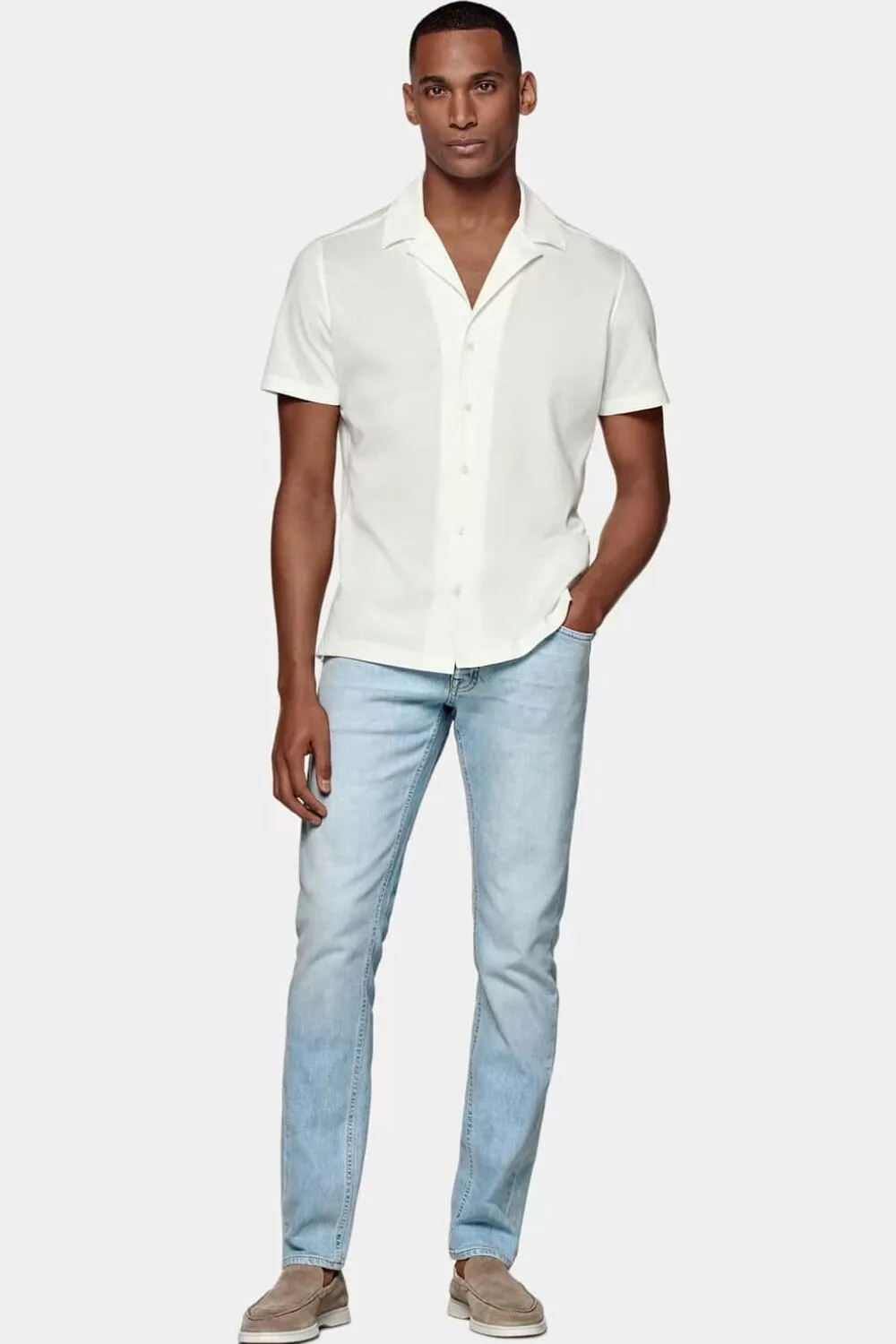 A man wearing well-fitted light-wash jeans, a crisp button-down, clean minimalist loafers, and simple accessories like a classic watch — a perfect summer outfit for a casual date night.