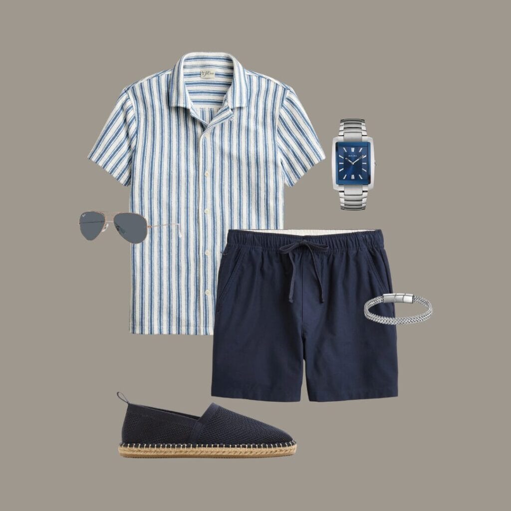 Men's casual summer outfit for vacation, brunch dates, or casual summer gatherings, featuring a white and blue striped camp collar shirt, navy drawstring shorts, navy espadrilles, a silver bracelet, a silver watch, and navy sunglasses.