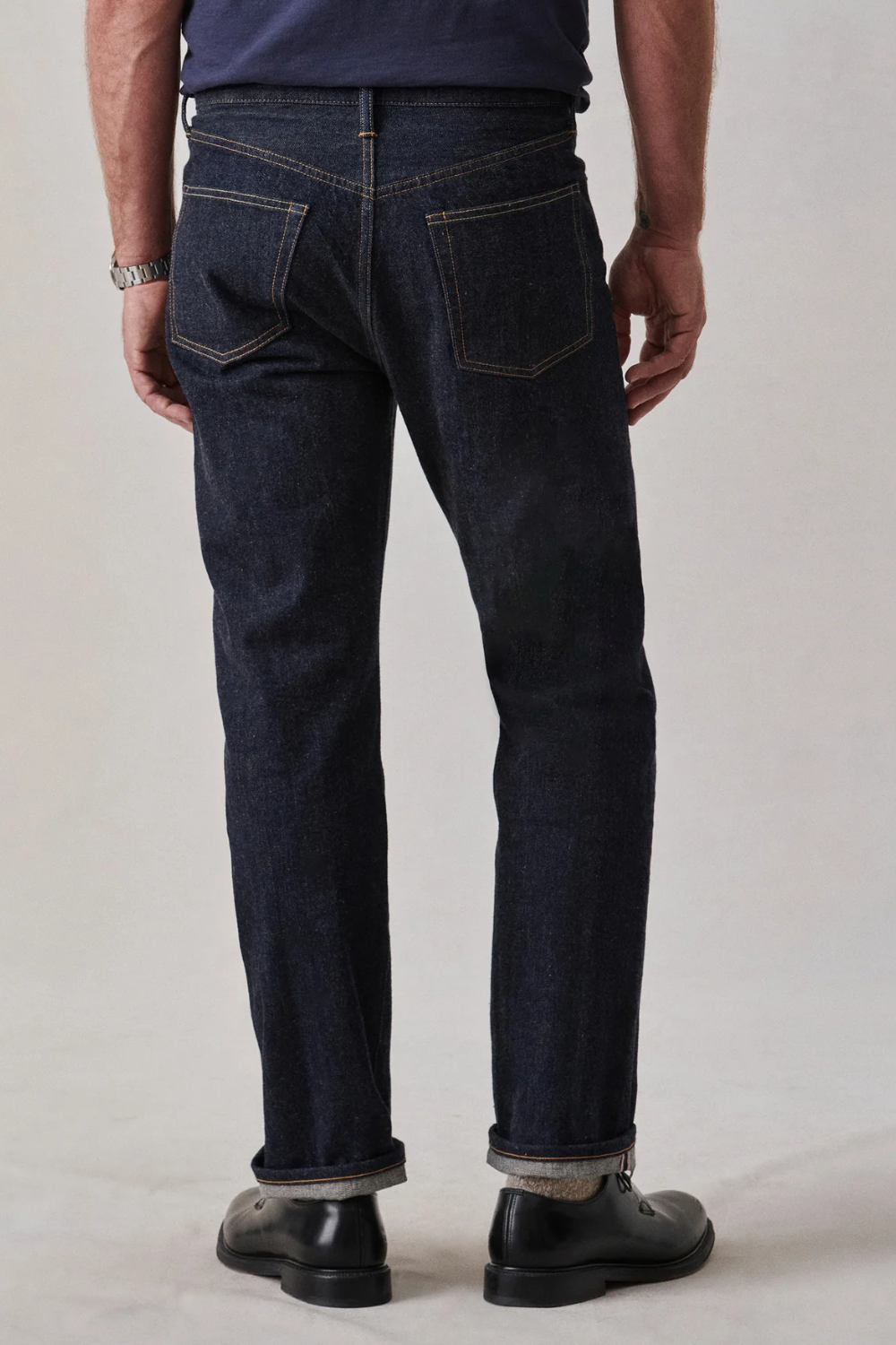 A man wearing Buck Mason Japanese Loomstate Selvedge Full Saddle Jeans in dark indigo, shown from the back.