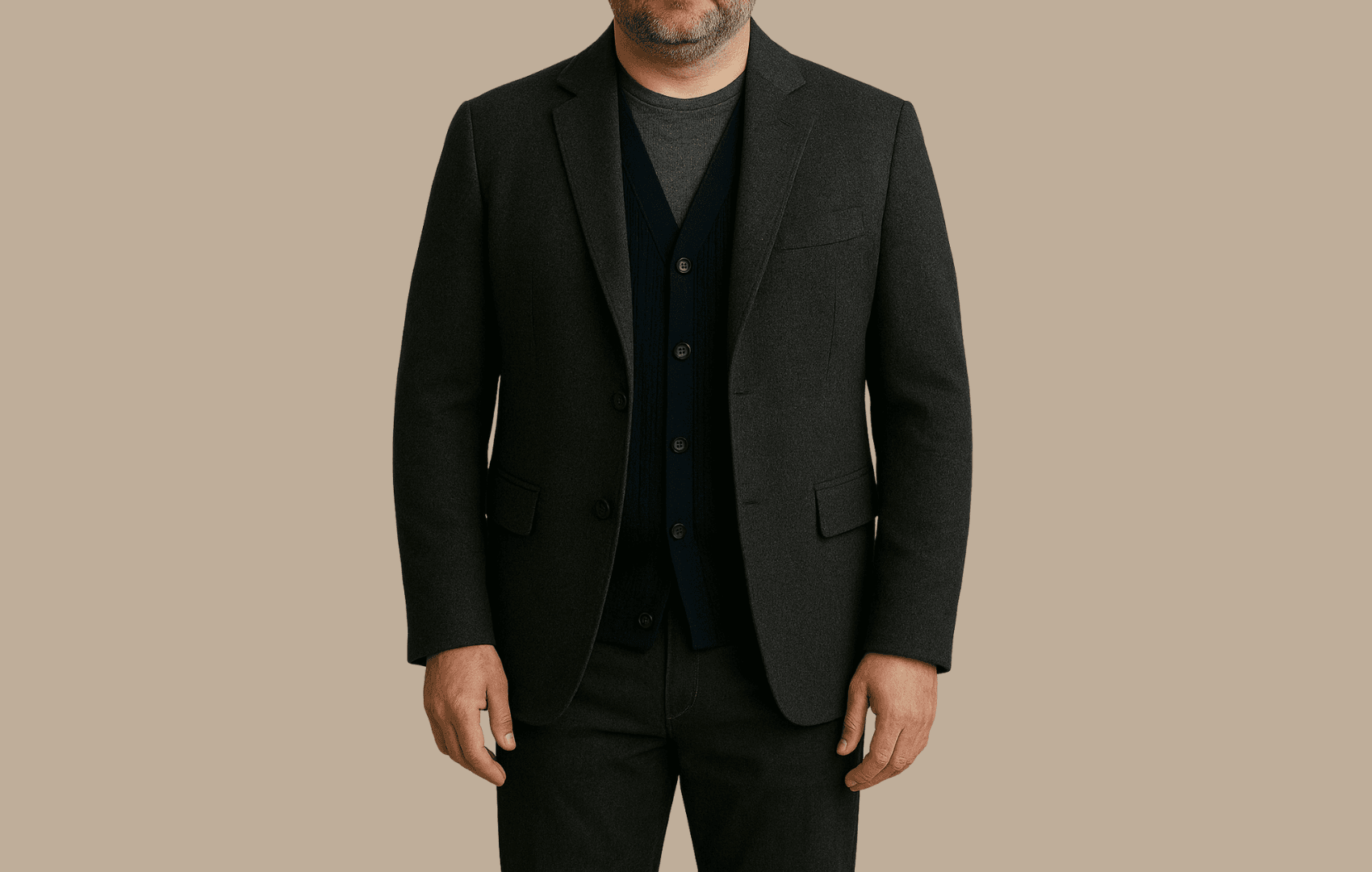 A middle-aged man with a dad bod wearing a charcoal wool sports coat over a navy cardigan and dark gray crewneck tee, shown from nose to waist against a beige background.