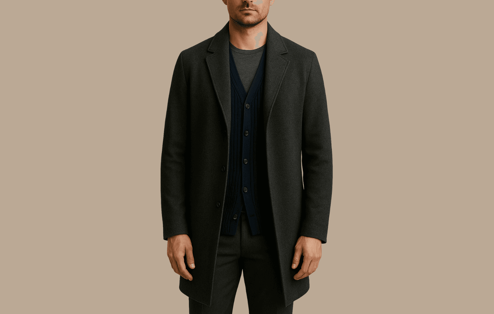 A man wearing a dark gray wool car coat over a navy ribbed cardigan and charcoal crew neck tee, shown from nose to knees against a beige background.