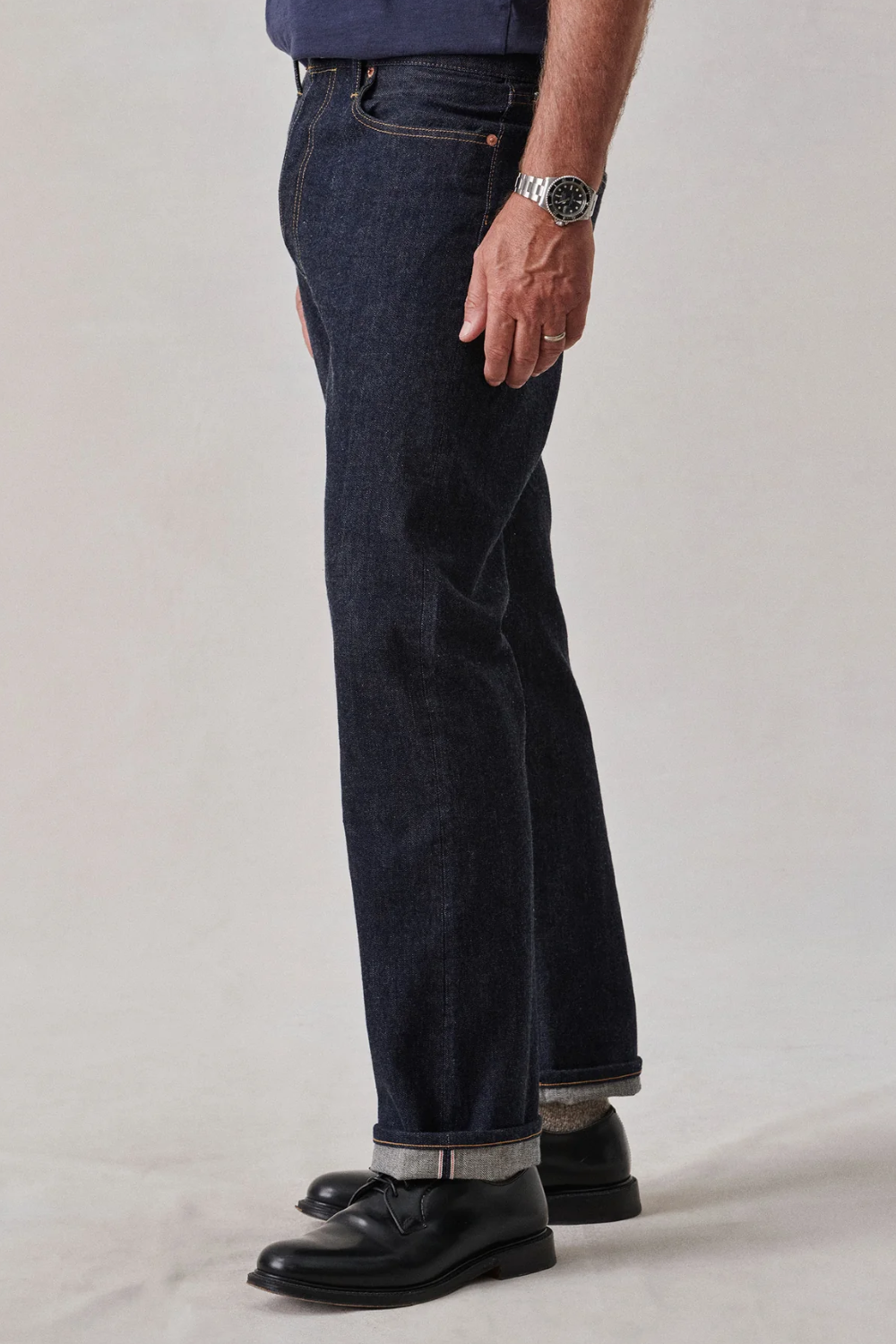 A man wearing Buck Mason Japanese Loomstate Selvedge Full Saddle Jeans in dark indigo, side view.