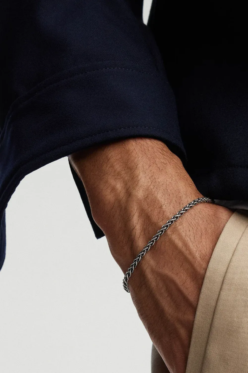 Close-up of a man’s hand in his pants pocket wearing the Mejuri 3.3mm Wheat Chain Bracelet, showing the sleek silver links catching soft light.