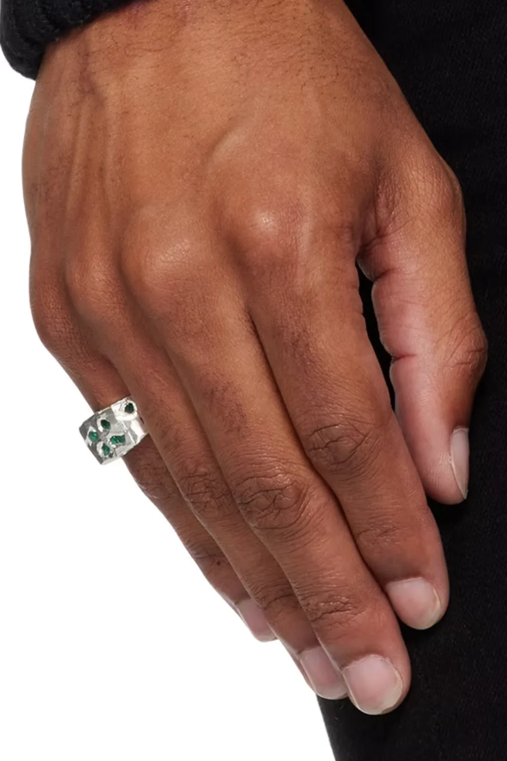 Close-up image of a man’s hand wearing The Ouze Raw Emerald Scatter signet ring, showcasing rough-cut emerald stones set unevenly across a textured silver surface.