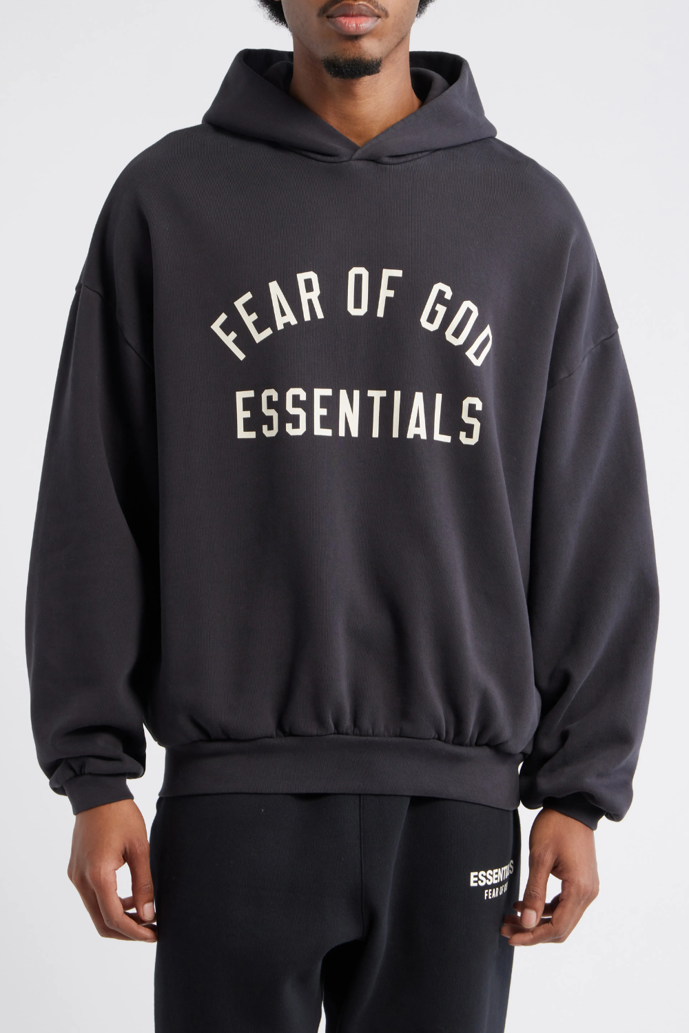 Man Wearing Fear of God Essentials '90s Fit Cotton Logo Hoodie in Black