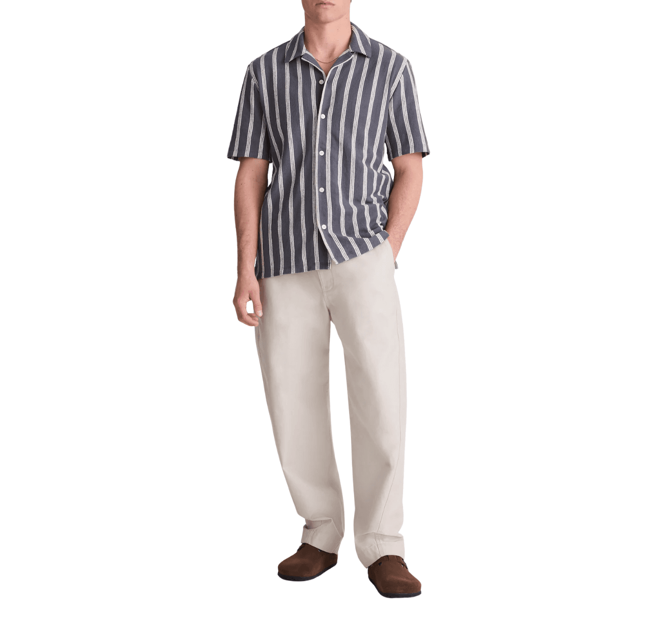 Man wearing a navy and white striped shirt with cream pants and brown Birkenstock shoes, standing with one hand in his pants pocket.