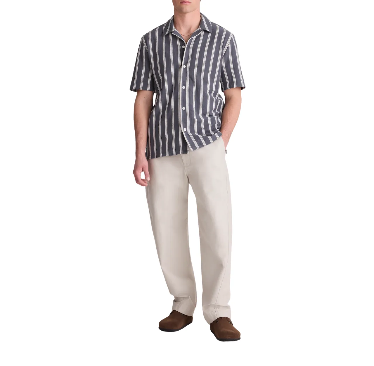 Man wearing a navy and white striped shirt with cream pants and brown Birkenstock shoes, standing with one hand in his pants pocket.