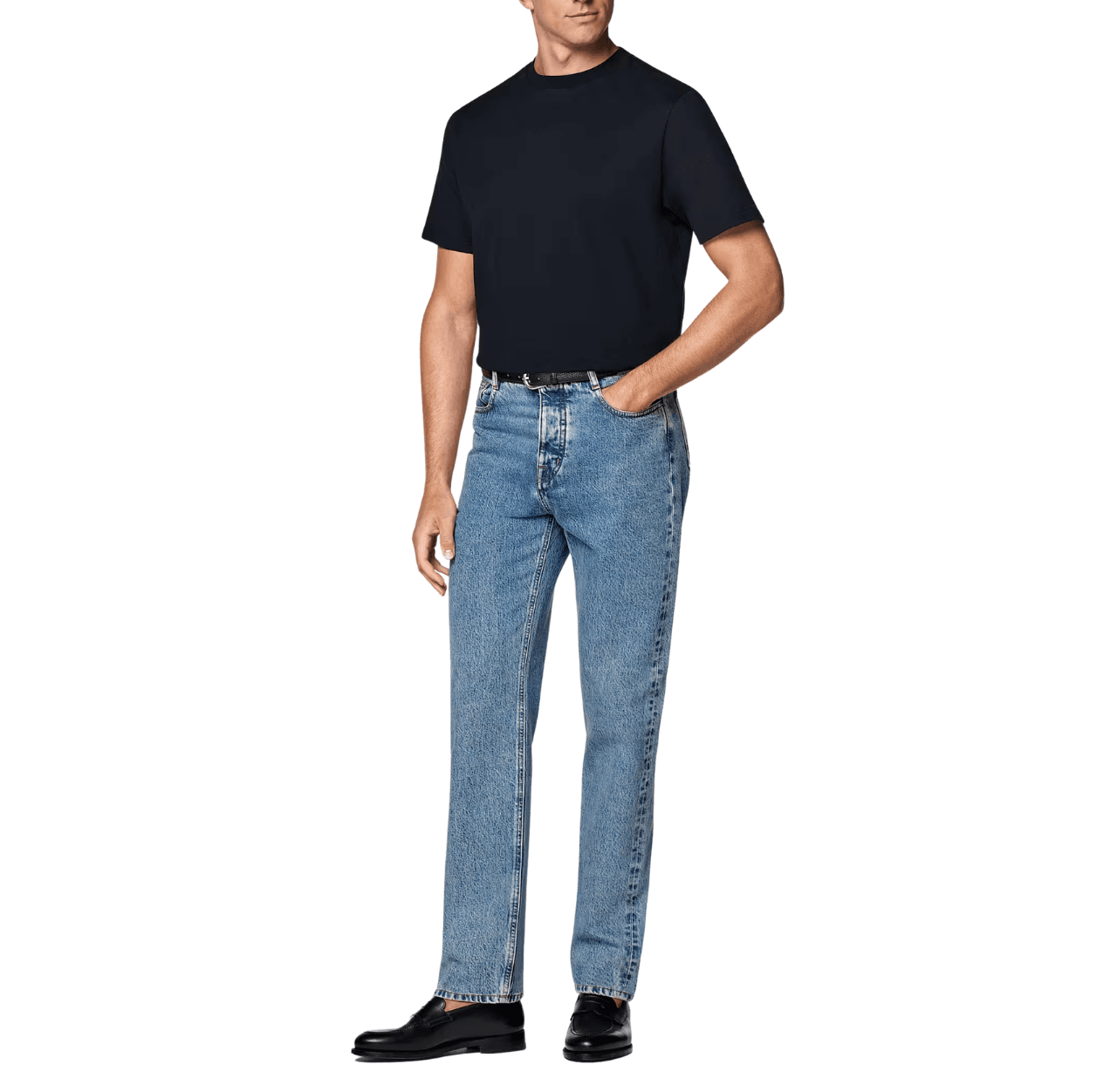 Man wearing a navy T-shirt with blue jeans and black leather loafers, standing with one hand in his pants pocket.