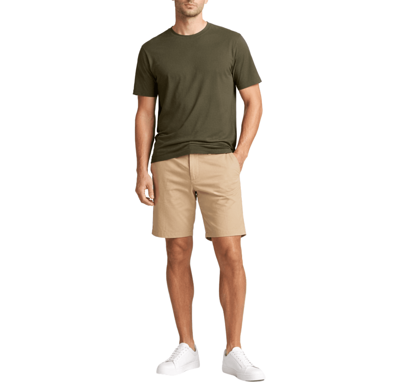 Man wearing an olive T-shirt with khaki shorts and white sneakers, standing casually with one hand in his shorts pocket.