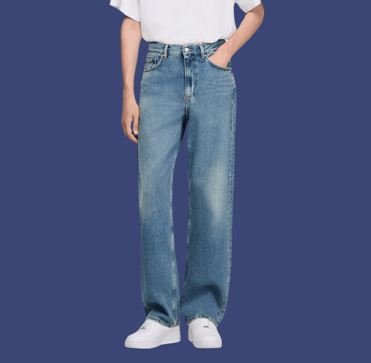 Man wearing blue baggy jeans and white chunky sneakers, standing casually with one hand in his pocket.