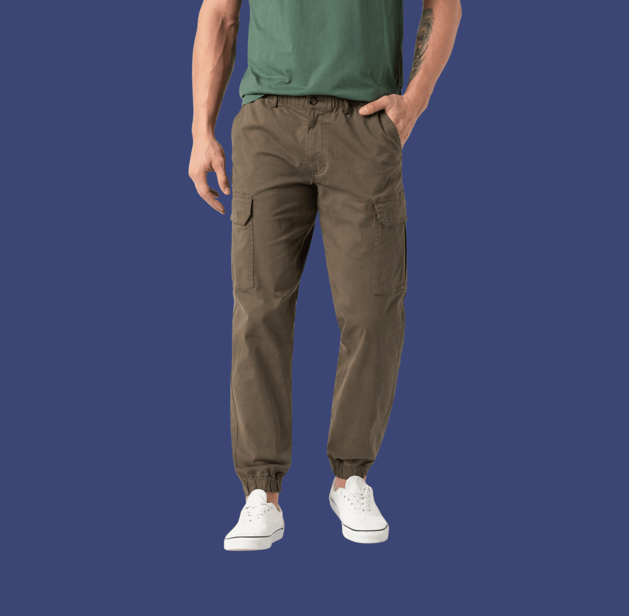Man wearing olive cargo joggers and white canvas sneakers, standing casually with one hand in his pocket.
