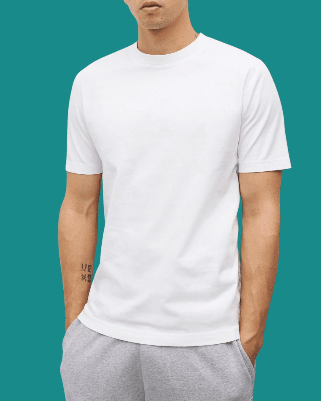 Man in Reigning Champ Midweight Jersey White T-Shirt with hands in pockets, standing casually.