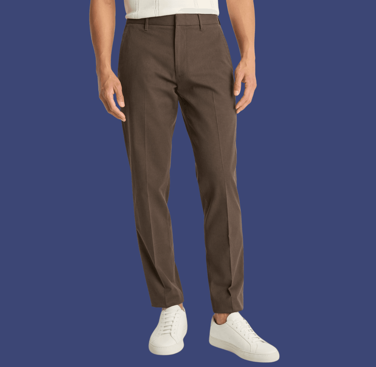 Man wearing brown slim dress pants and white leather low-top sneakers, standing casually with arms relaxed at his sides.