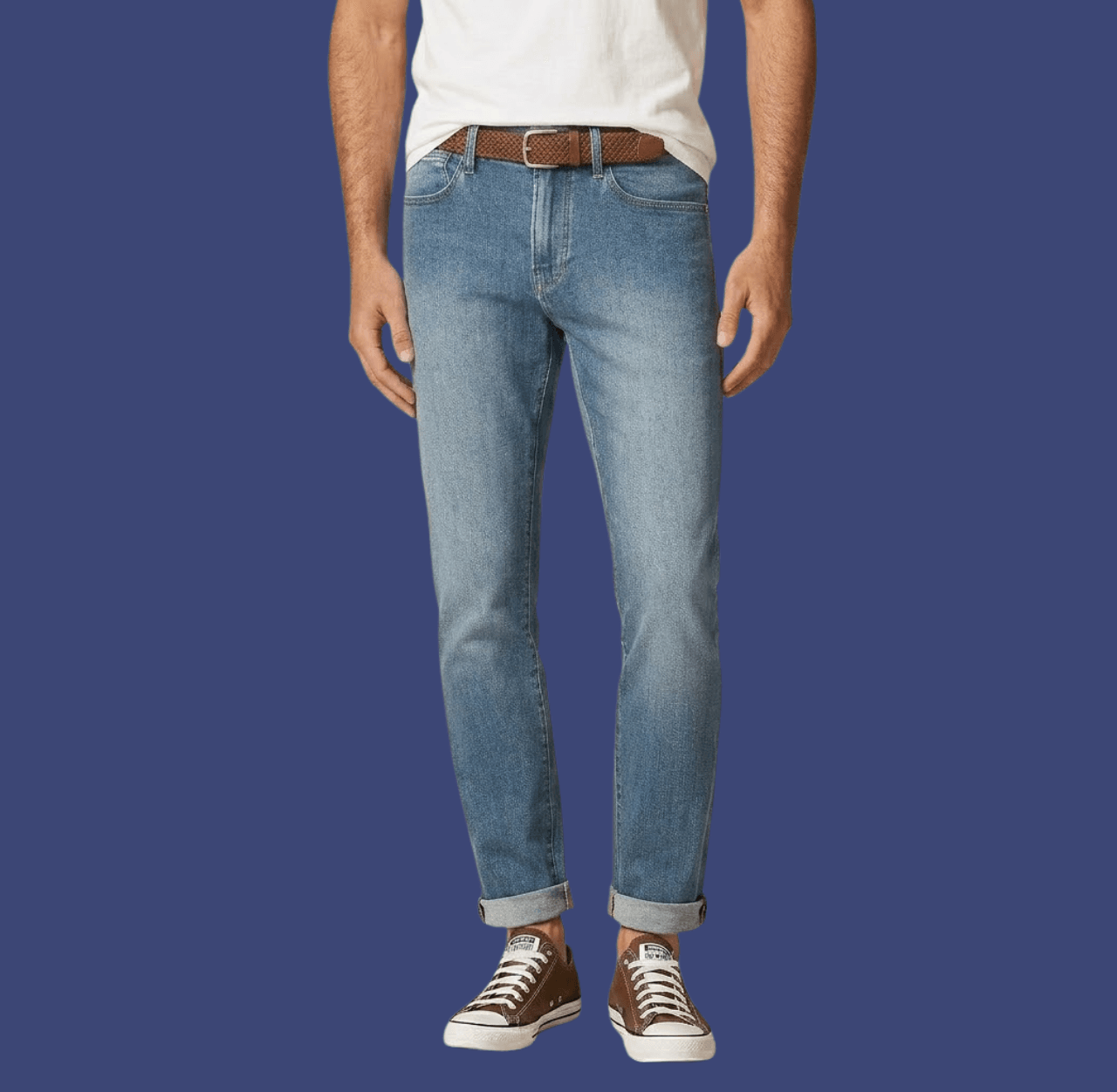 Man wearing cuffed blue slim-fit jeans and brown Converse canvas sneakers, standing casually with arms relaxed at his sides.