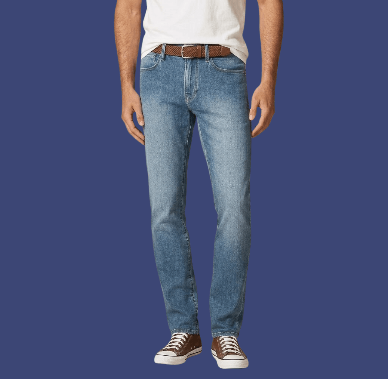 Man wearing uncuffed blue slim-fit jeans and brown Converse canvas sneakers, standing casually with arms relaxed at his sides.