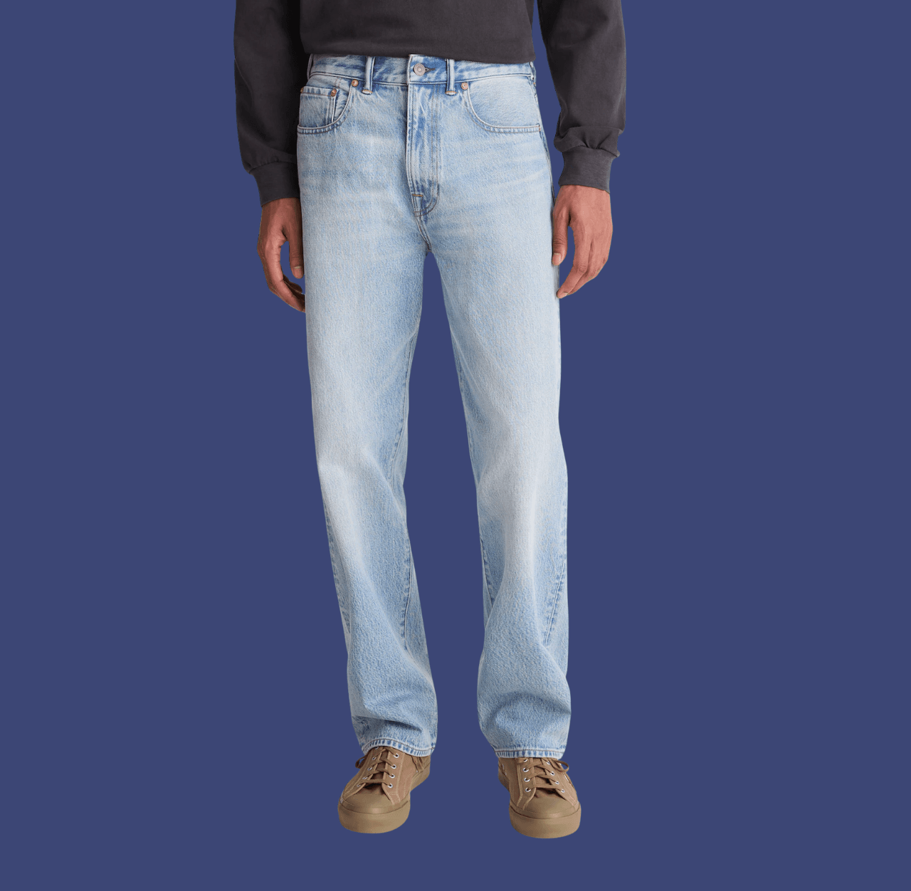 Man wearing blue straight-fit jeans and brown low-top sneakers, standing casually with arms relaxed at his sides.