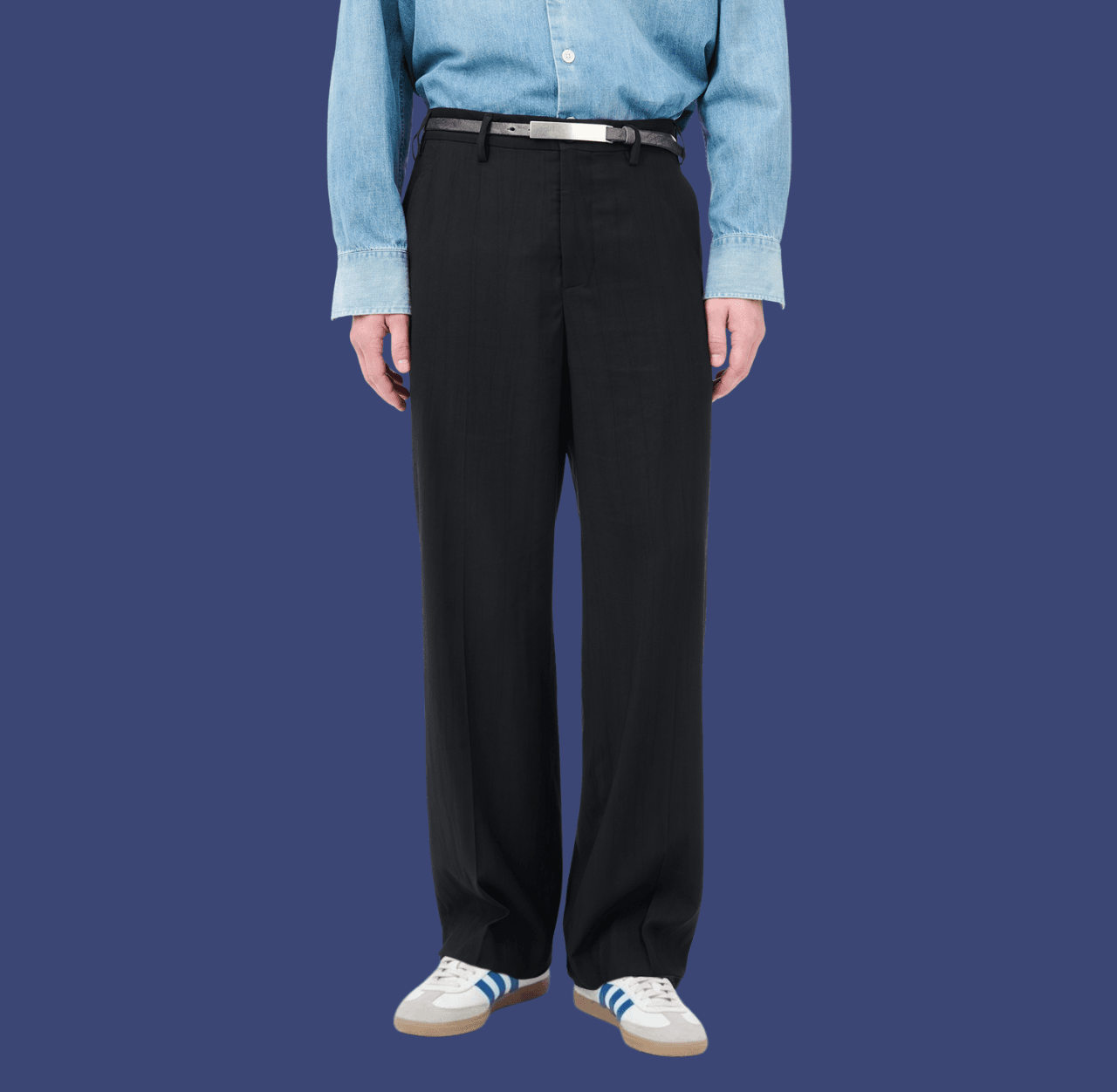 Man wearing black wide-leg dress pants and white leather low-top sneakers, standing casually with arms relaxed at his sides.