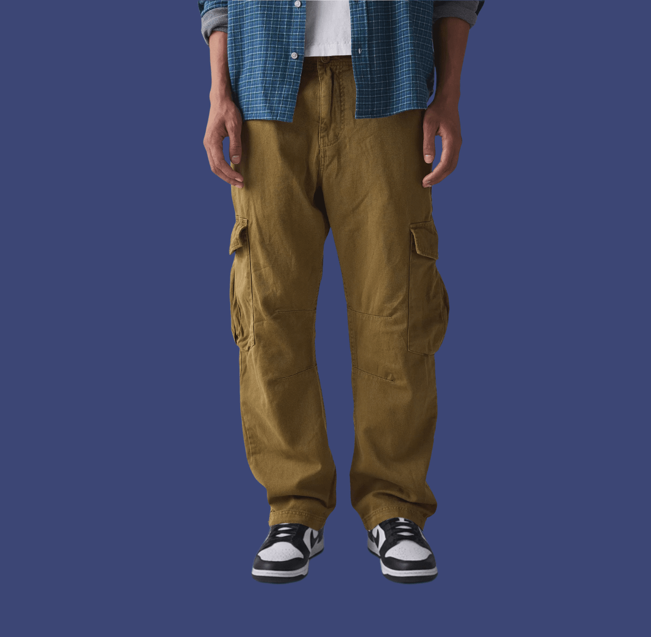 Man wearing yellow brown relaxed cargo pants and black low-top sneakers, standing casually with arms relaxed at his sides.