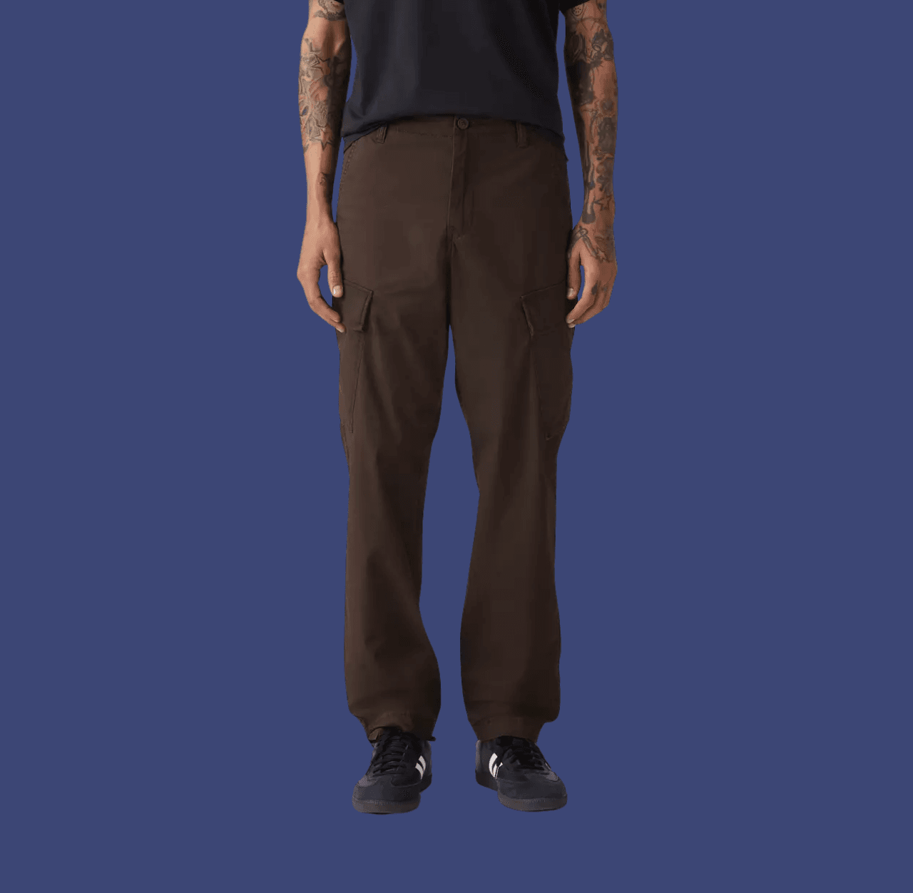 Man wearing brown tapered cargo pants and black low-top sneakers, standing casually with arms relaxed at his sides.