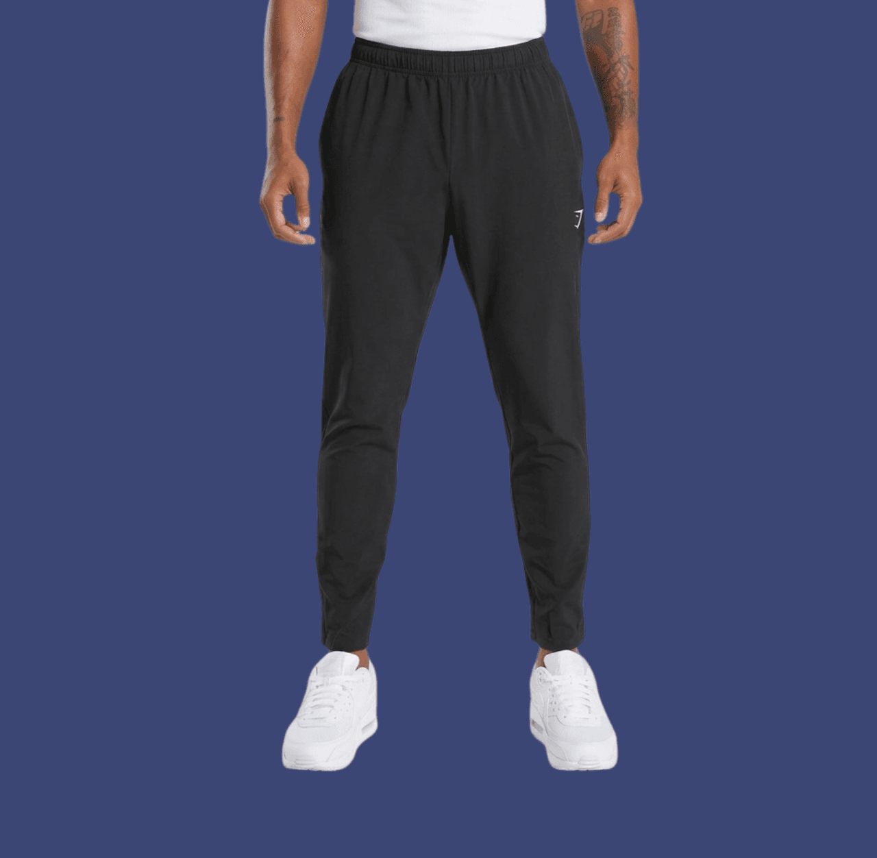 Man wearing black tapered joggers and white Nike Air sneakers, standing casually with arms relaxed at his sides.