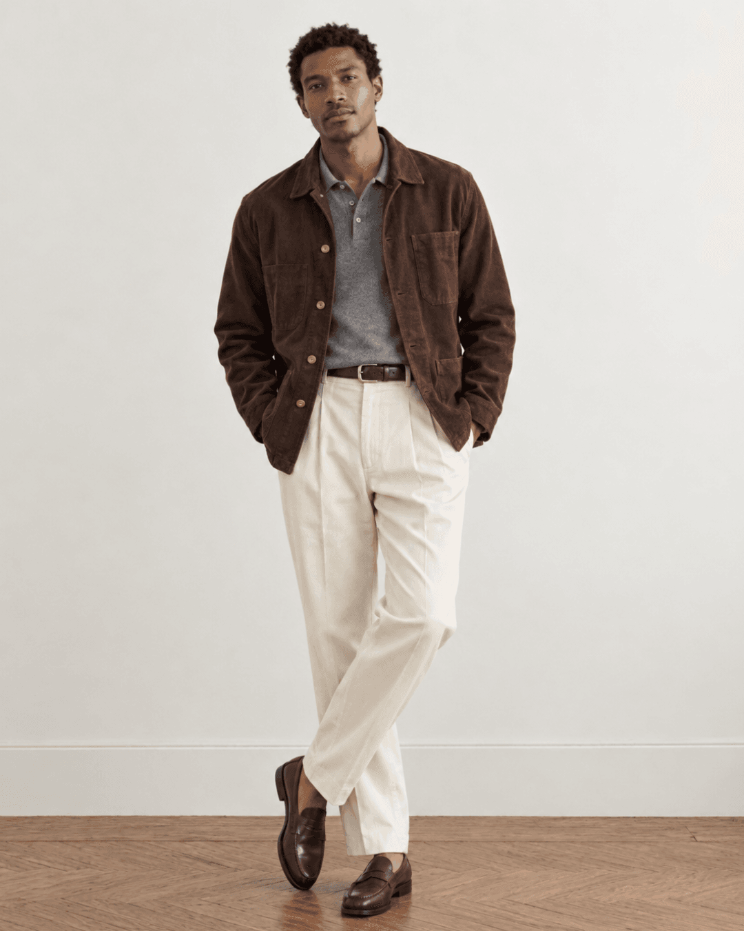 Man wearing a Chocolate brown chore coat, a Gray knit polo, Ecru pleated trousers, and Burgundy suede loafers