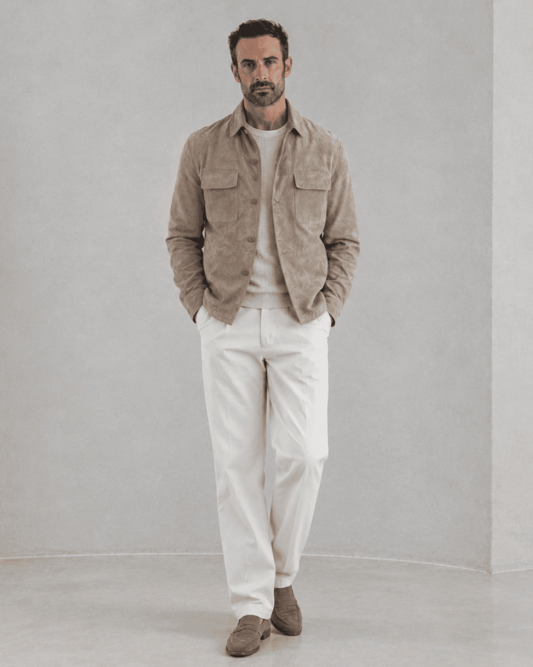 Man wearing a suede shirt jacket, a knit sweater, white chinos, and suede loafers