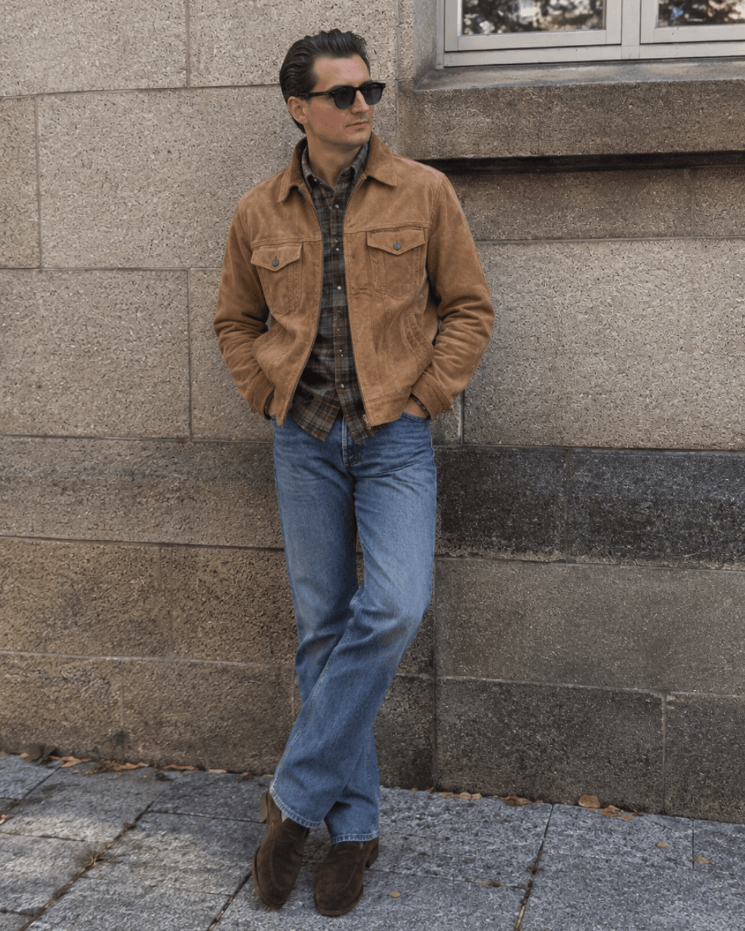 Man wearing a suede western jacket, a flannel shirt, medium wash jeans, and suede penny loafers