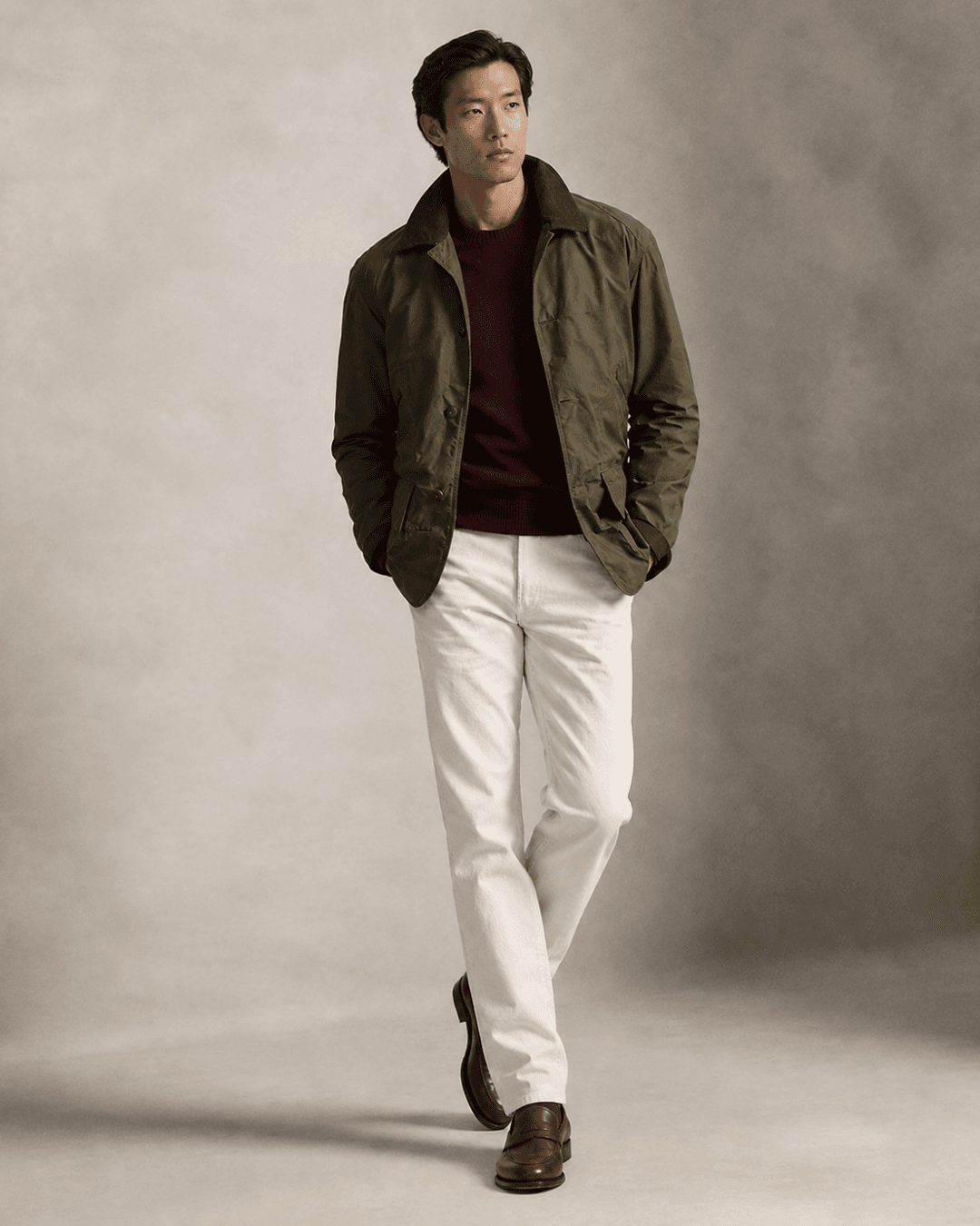 Man wearing an Olive field jacket, a Burgundy merino crewneck, Ecru jeans, and Dark brown leather loafers