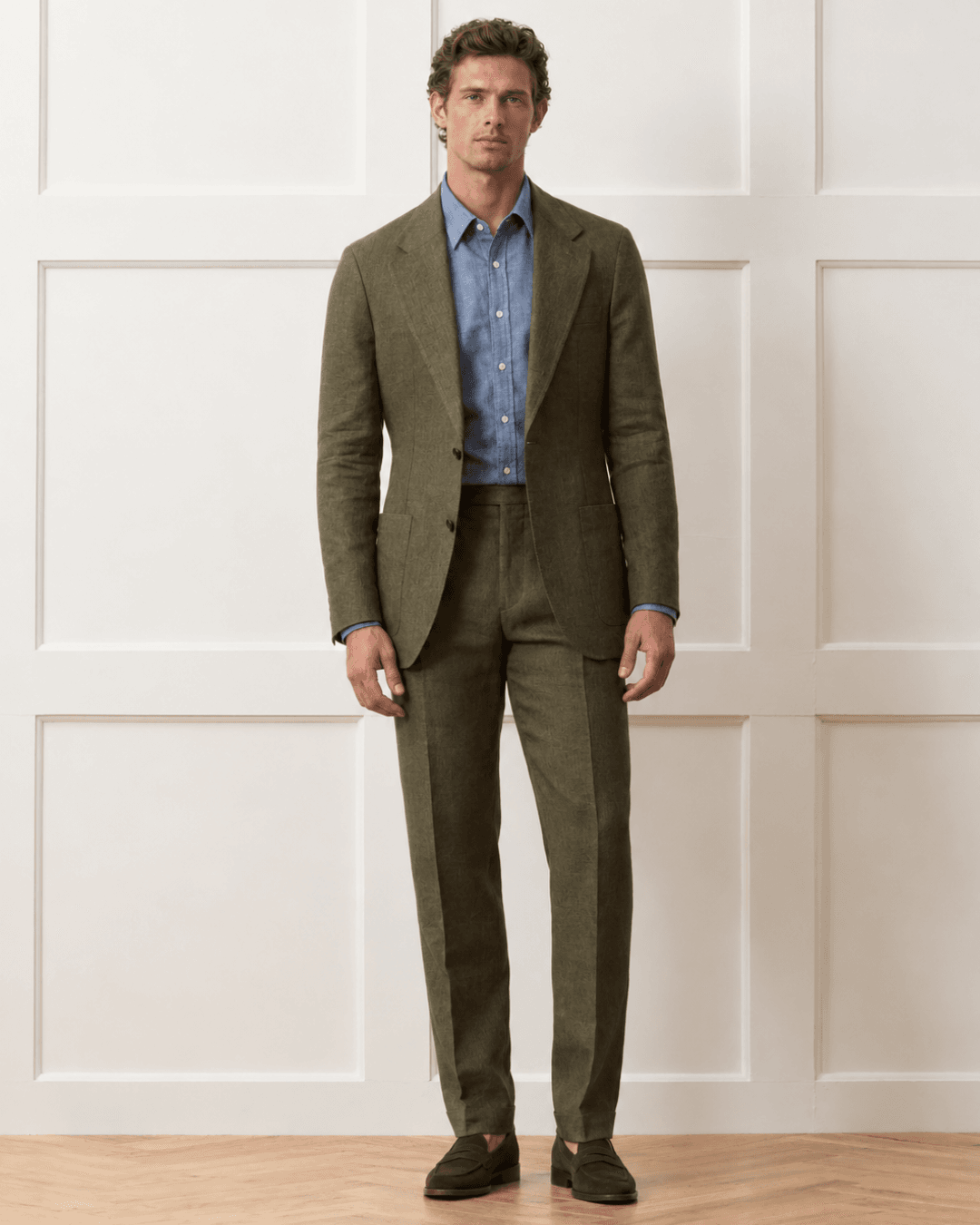 Man wearing a Dark Olive Unstructured Suit, a Chambray Shirt, and Loafers