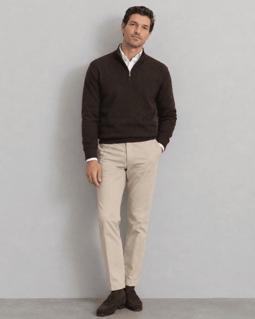Man wearing an Olive field jacket, a Burgundy merino crewneck, Ecru jeans, and Dark brown leather loafers